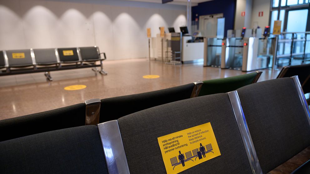 Tomt väntrum på en flygplats med avståndsskyltar på sittplatserna. En informationsskylt på en av bänkarna visar rekommendationer för avstånd mellan passagerare för att förhindra spridning av smitta.