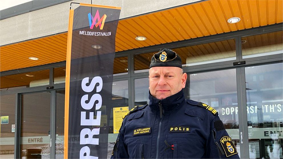 En polisuniformerad person står utanför en byggnad med ett ”PRESS”-flaggstång i bakgrunden.