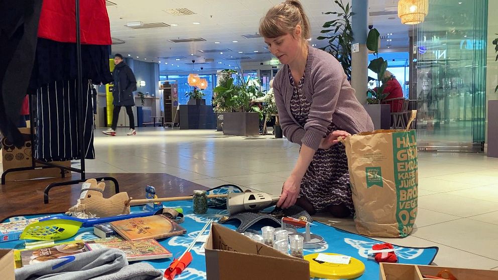 En kvinna lägger ut leksaker på en matta i ett köpcentrum.