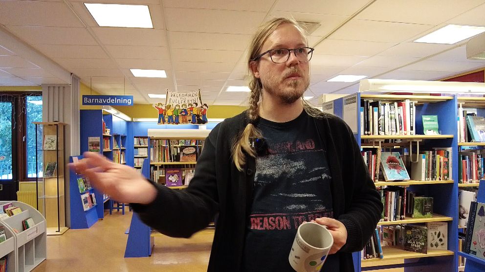 En bibliotekarie står med en kopp i den ena handen och håller ut den andra handen