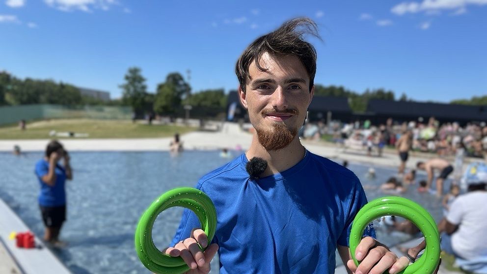 En man står med badringar framför en utomhuspool