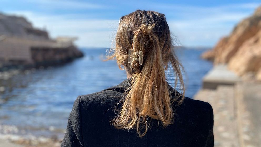 Kvinna står bortvänd från kameran mot havet