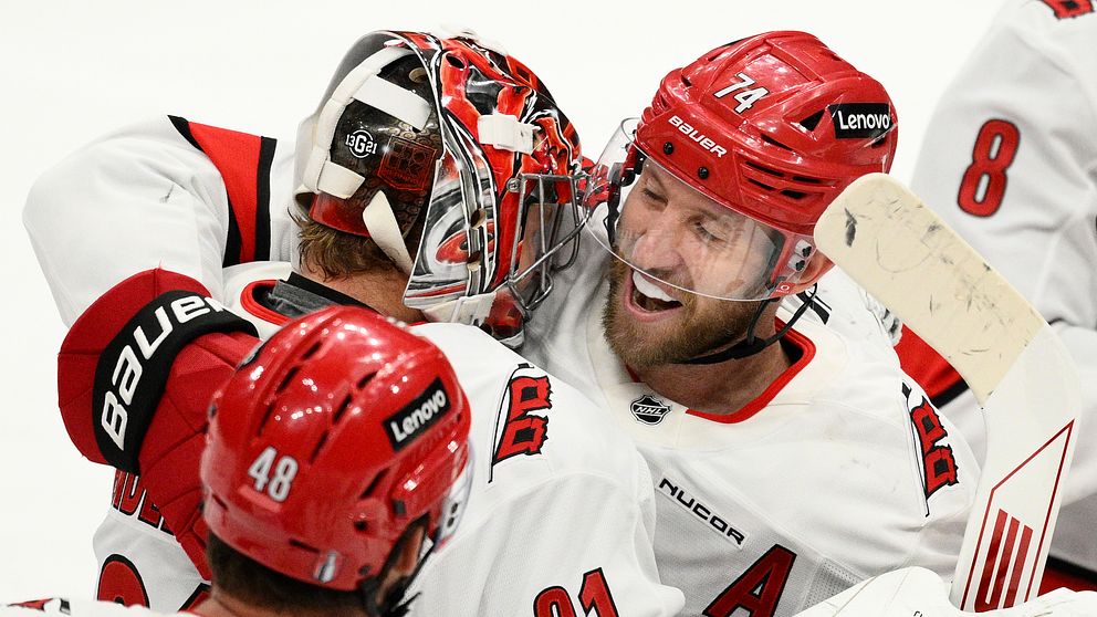 Ishockeyspelare i rödvita matchställ kramar om varandra och firar på isen.