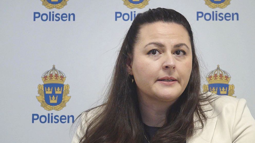 Kvinna sitter framför en vägg med svenska polisens logga.