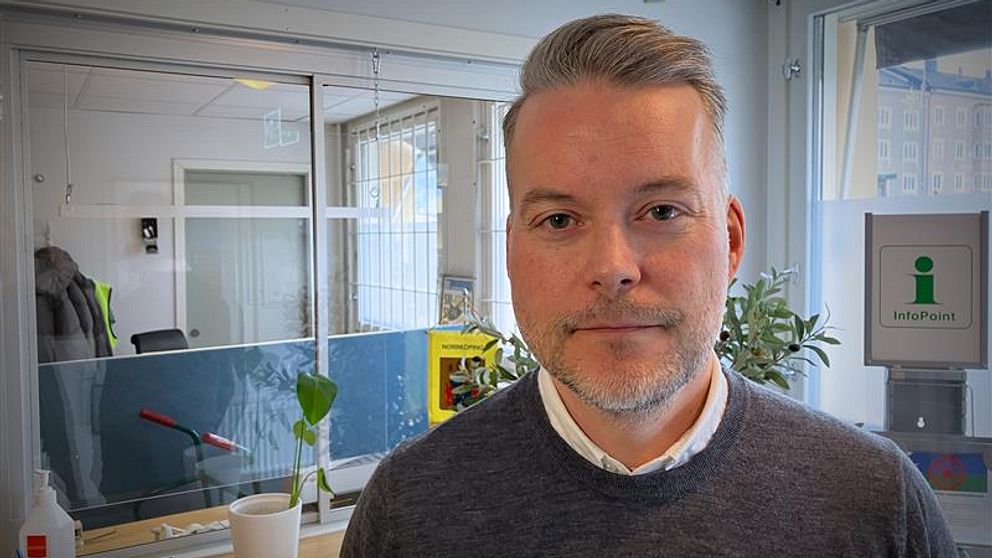 Jonas Eriksson syns en receptionsdisk med några plantor och kontorsmaterial samt en glasvägg med en öppen dörr i bakgrunden.