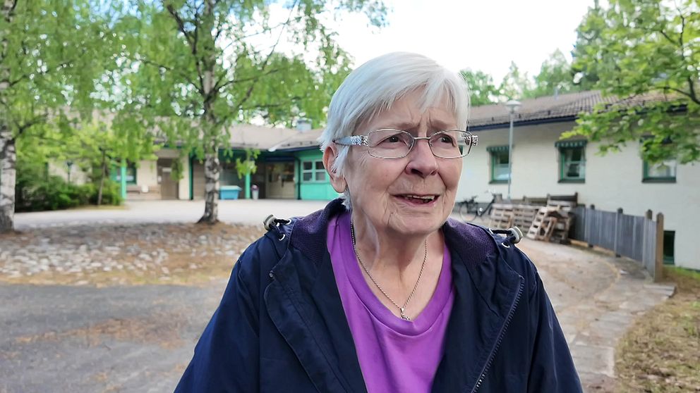 Kvinna med grått hår och glasögon står framför en hälsocentral.