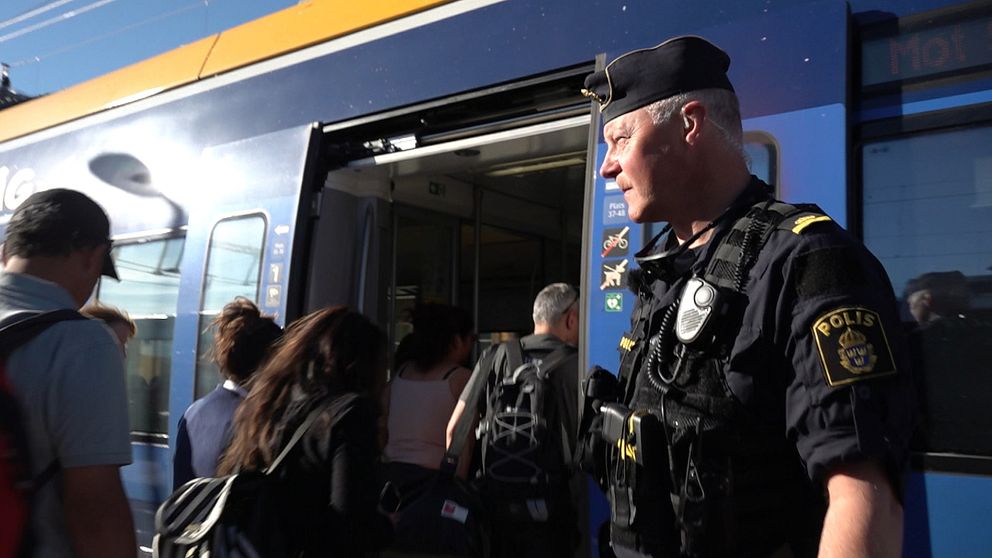 Polis står på perrong och passagerare på väg in på tåg