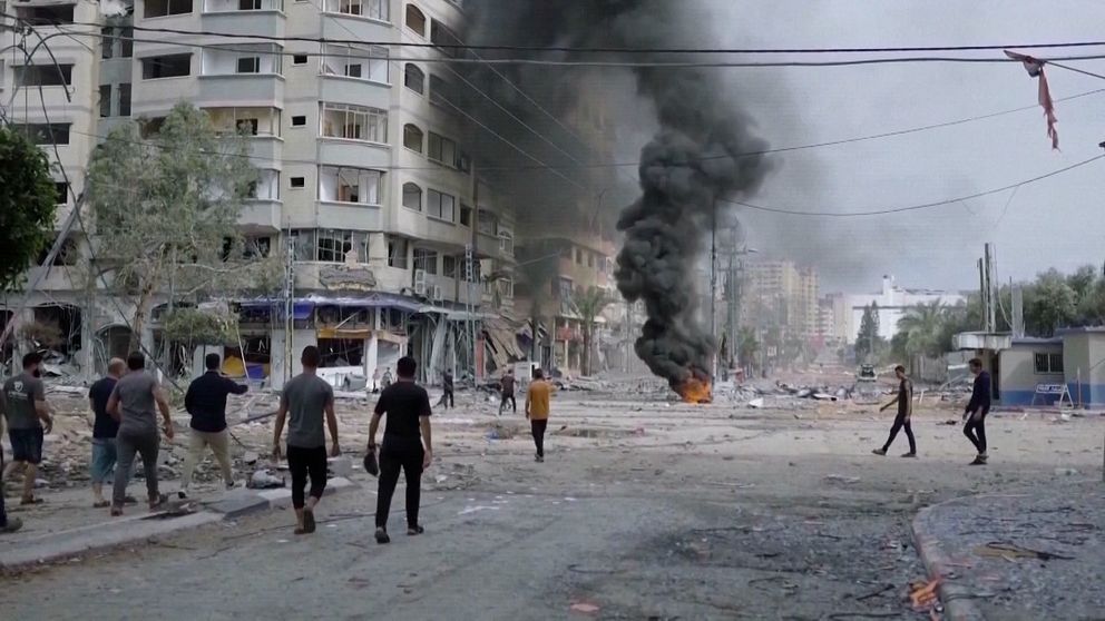 Människor går på gata i Gaza där eld och rök syns.