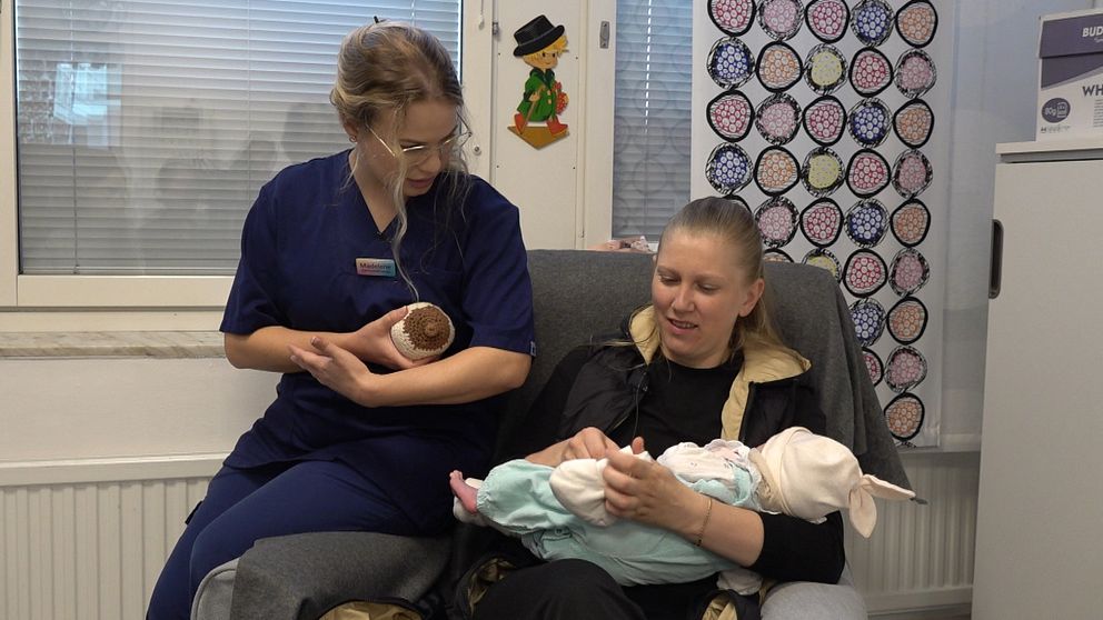 mamma håller i sin bebis, barnmorska sitter bredvid och instruerar om amning