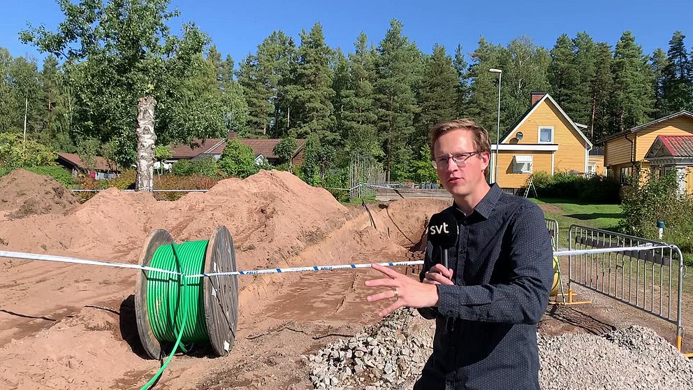 En man med mikorfon står framför en grop som är avspärrad av polisen