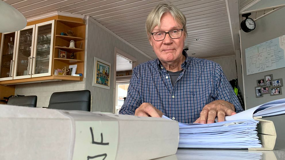 Gunnar Holmberg sitter vid köksbordet. Framför sig har han en pärm full med viktiga dokument.