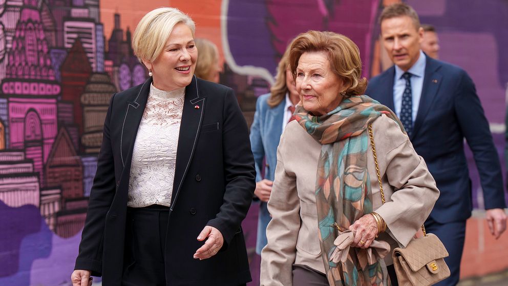 Personer promenerar framför en färgglad väggmålning. En annan man följer efter.