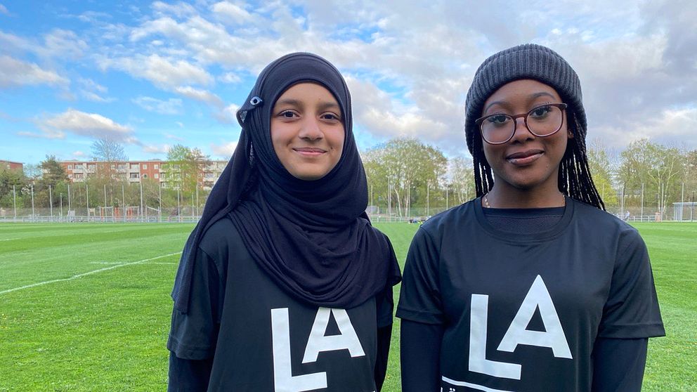 Två tjejer i träningskläder står på en fotbollsplan