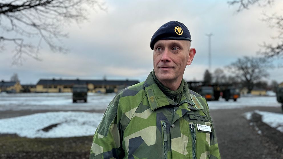 Regementeschefen Per Åkerblom, man klädd i militärkläder, tittar snett in mot kameran. Militära fordon i bakgrunden.