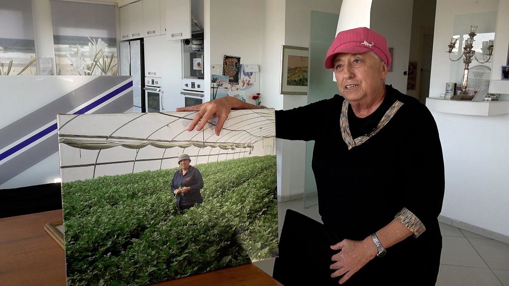 Anita Tucker håller upp ett foto på sig själv. På fotot står hon i ett stort växthus omgiven av plantor.