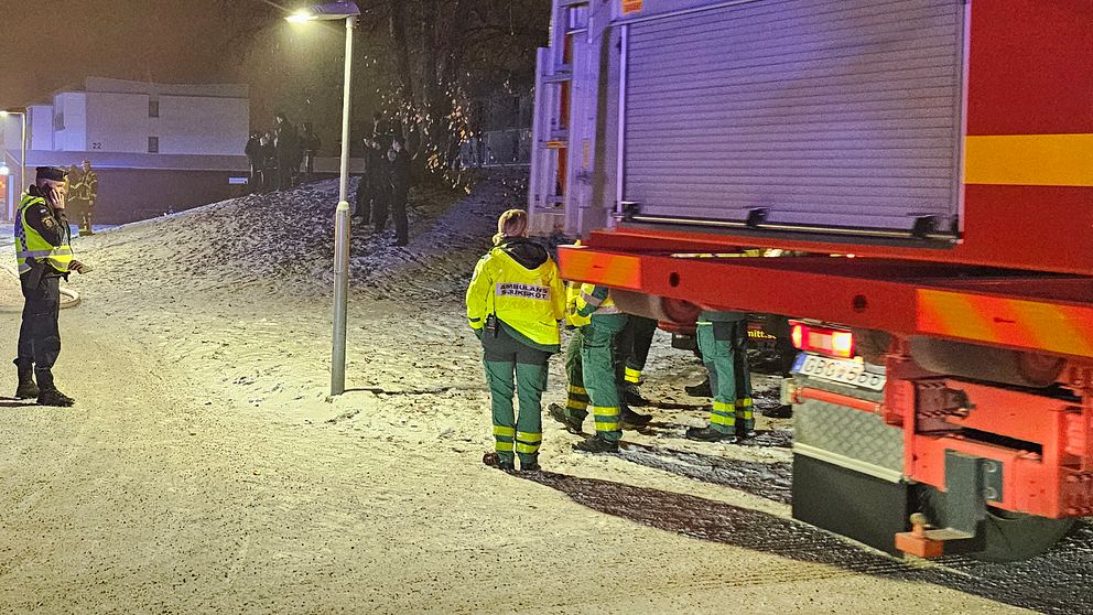 en brandbil, räddnignstjänsten och en polis. i bakgrunden syns människor och byggnader.