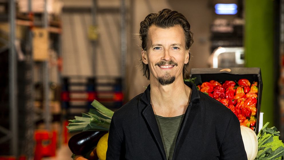 Paul Svensson står iklädd grön t-tröja och mörk kavaj. Bakom honom skymtas grönsaker i ett kök.