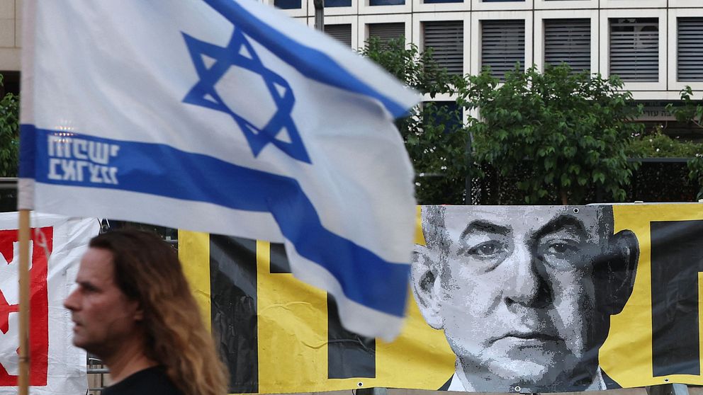 Person håller en israelisk flagga framför en avbildning av den israeliska premiärministern Benjamin Netanyahu.