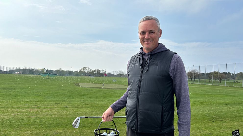 En person står på en golfbana och håller en korg med golfbollar.