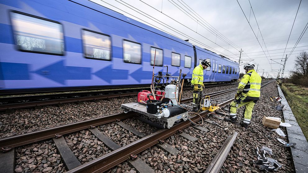 Två arbetare från trafikverket lagar räls på järnväg