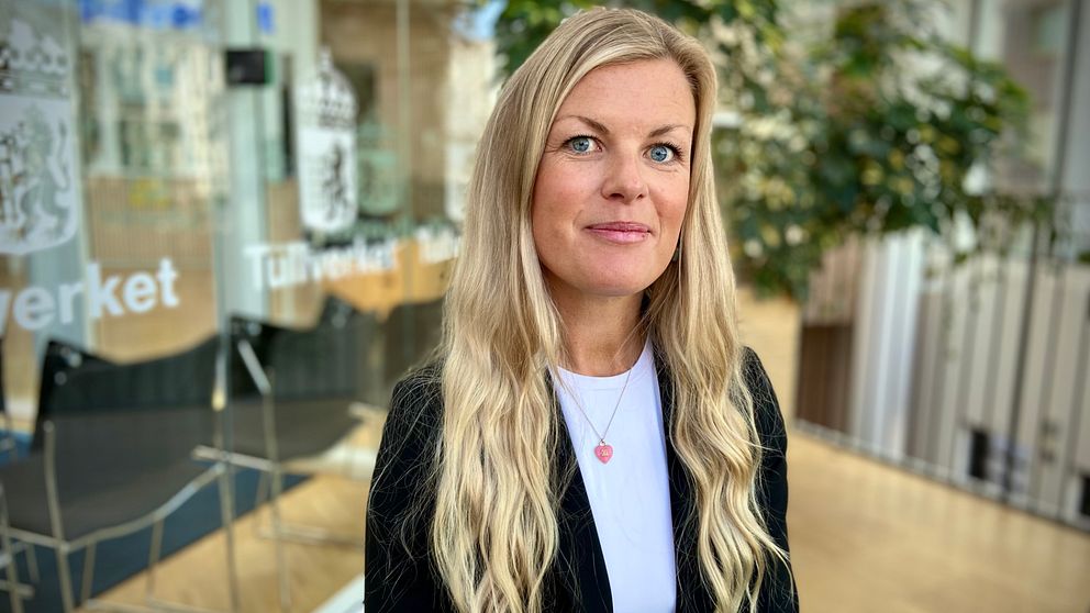 Kvinnlig Tullchef med långt blont hår står framför Tullverkets ingång.