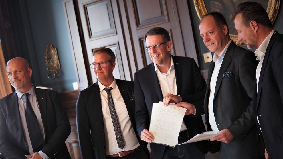 Män står står på rad och håller upp ett kontrakt.