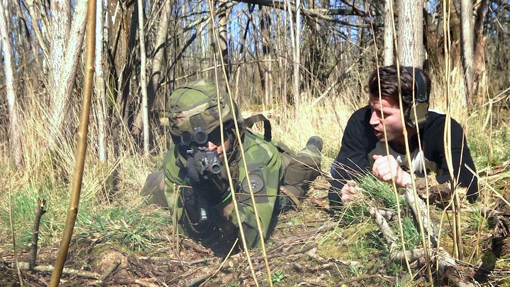 Kamouflerad soldat ligger i buskage under övning i skogen.