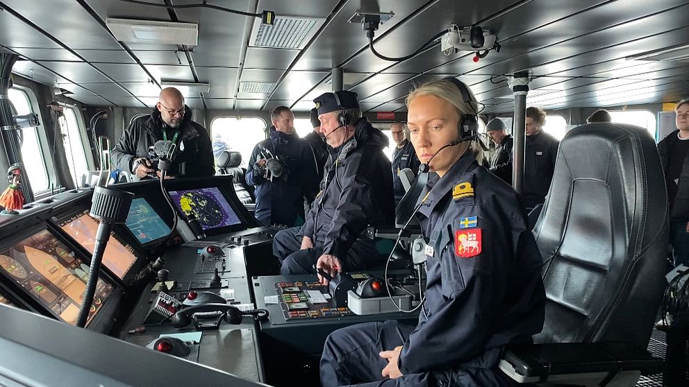 Besättningsmedlemmar i uniformer arbetar i kommandobryggan på ett fartyg, omgivna av avancerad navigationsutrustning och olika kontroller.