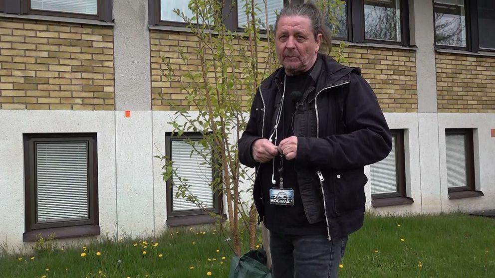 Person med ID-bricka står utomhus framför en byggnad med gula tegelväggar och fönster.