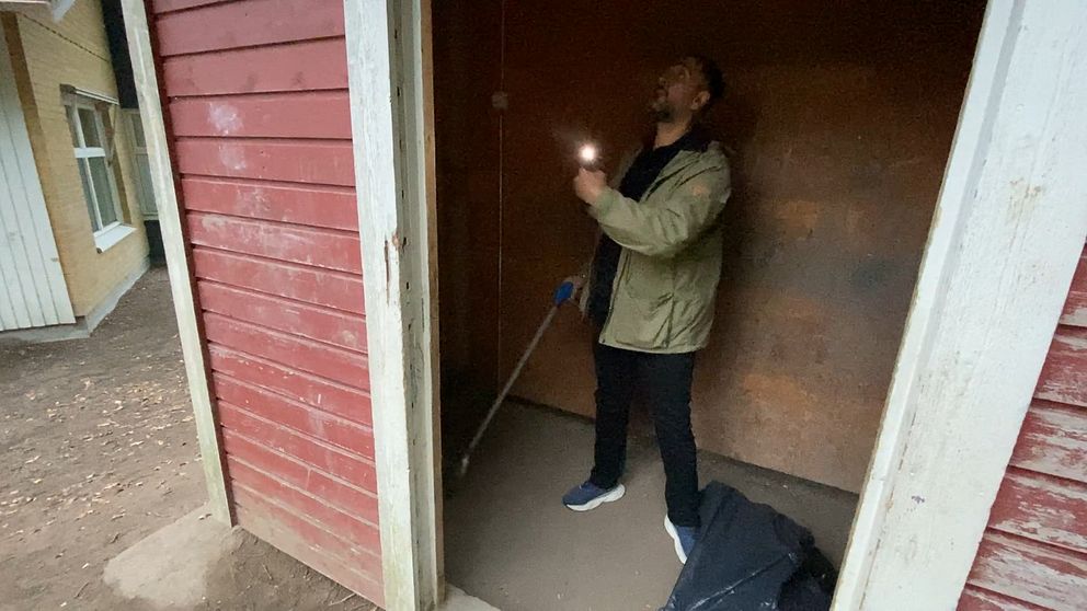 Oscar Tunedal, fritidspedagog på Blåsboskolan i Västerås lyser med en ficklampa i en av skolgårdens byggnader.