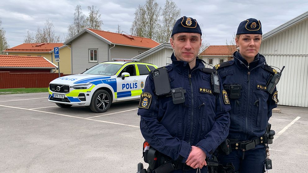 En manlig och en kvinnlig polis står framför sin polisbil