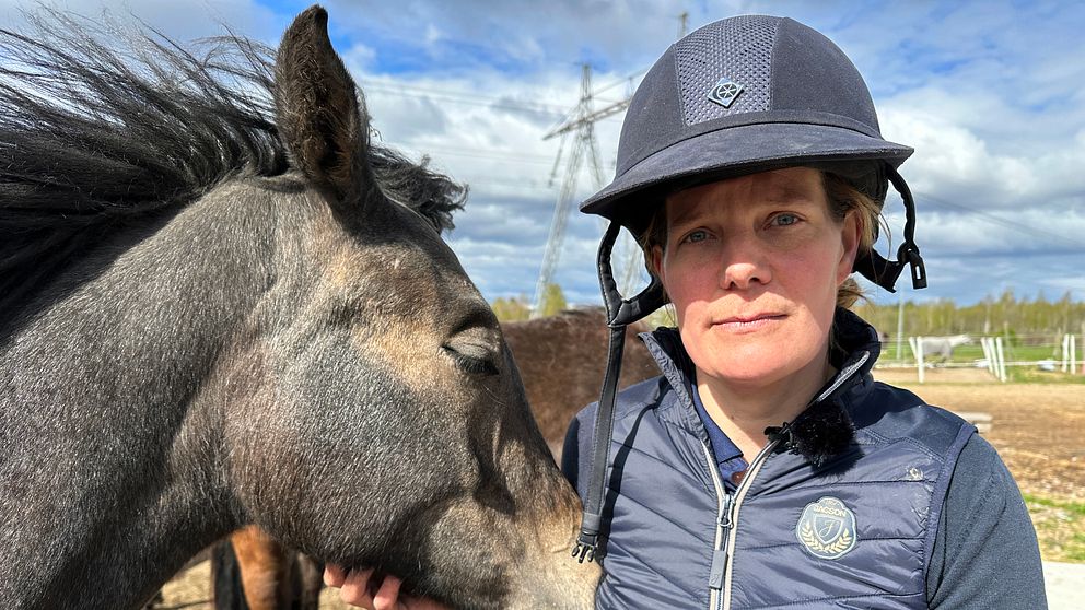 En person med ridhjälm står nära en häst som nosar mot personens axel utomhus.