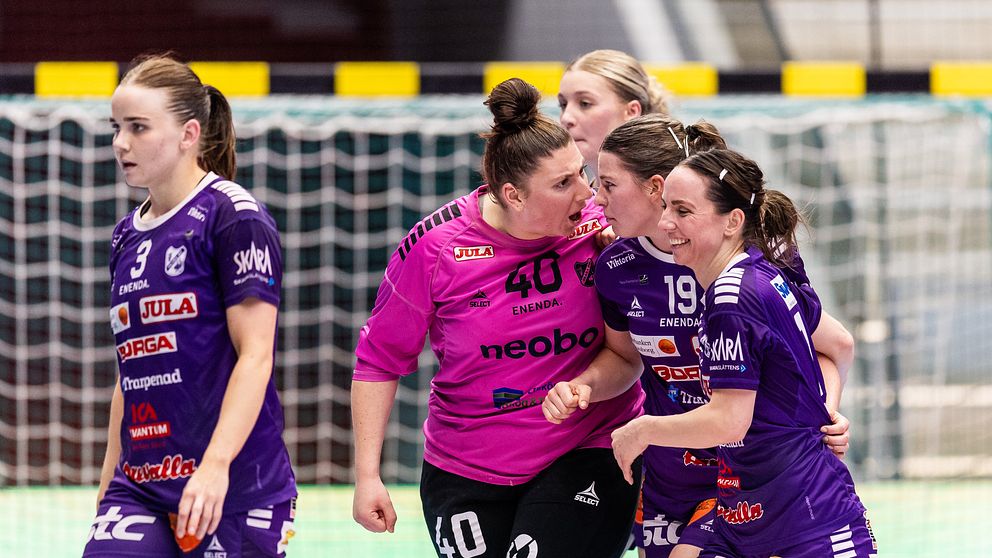 Fyra handbollsspelare samlas vid målet under en match i en inomhushall.