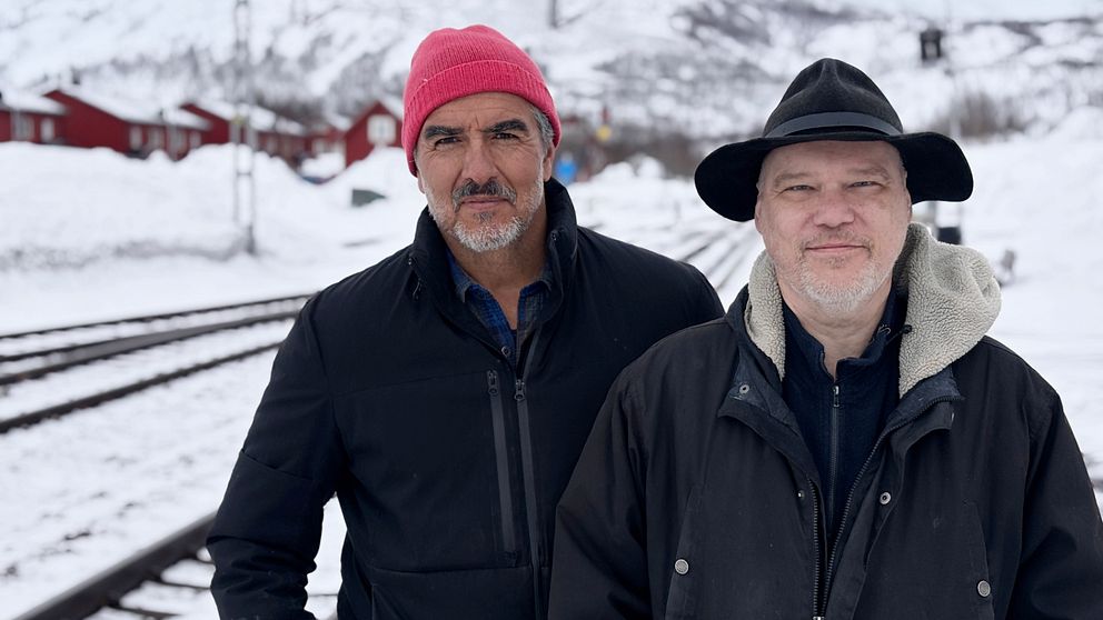 Rafael Edholm och Björn Olofsson, författare till romanen Svarta Björn, står bredvid varandra vid snötäckta järnvägsspår och röda hus.