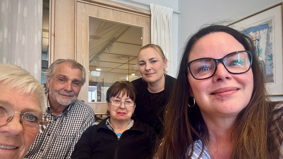 Fem personer sitter tillsammans inomhus framför ett fönster och en tavla.