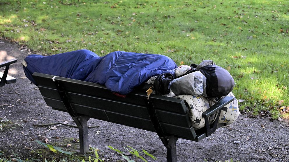 En person som sover ute på en parkbänk