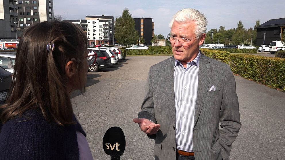 En man med grå kostym står på en parkering och pratar