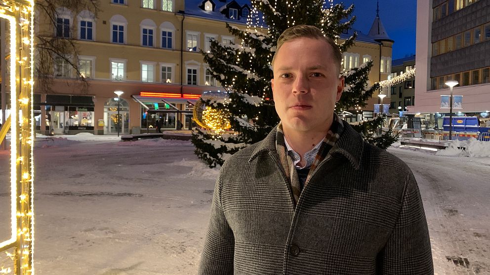 Det socialdemokratiska regionråd i Region Dalarna, Sebastian Karlberg, står utomhus framför en stor julgran.