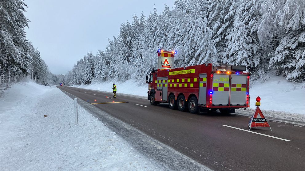En räddningstjänstbil som står på E18, vid sidan av vägen syns snöiga träd
