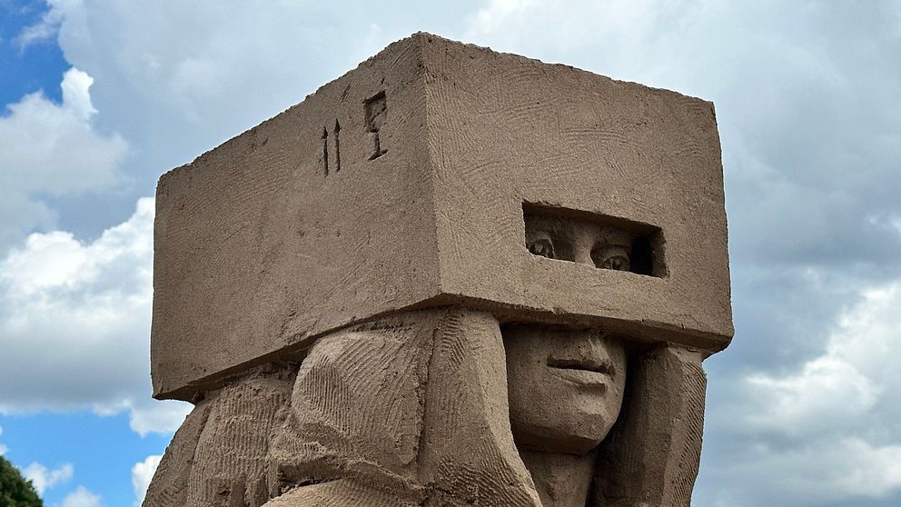 Sandskulptur i närbild. Ansikte med låda som täcker näsa.