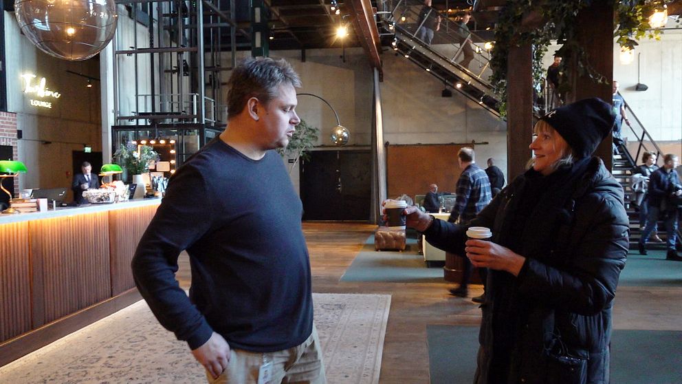 SVT:s reporter håller två pappmuggar med kaffe framför sig och erbjuder den ena till politikern från Köping.