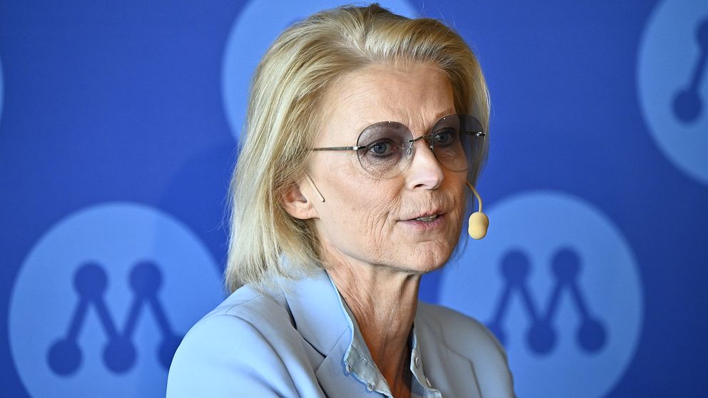 Elisabeth Svantesson (M) framför en blå bakgrund med Moderaternas logotyp.