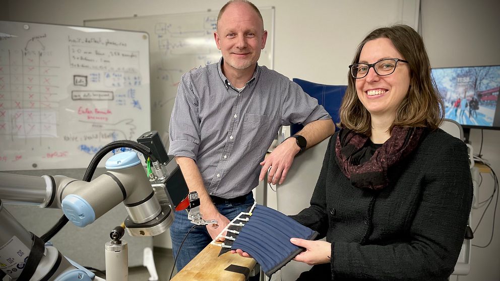 Två personer diskuterar vid en robotarm i ett laboratorieutrymme.