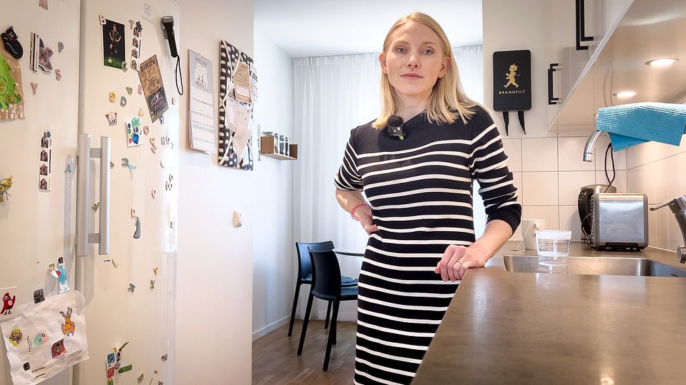 Person i randig klänning står i modernt kök med kylskåpsmagneter.