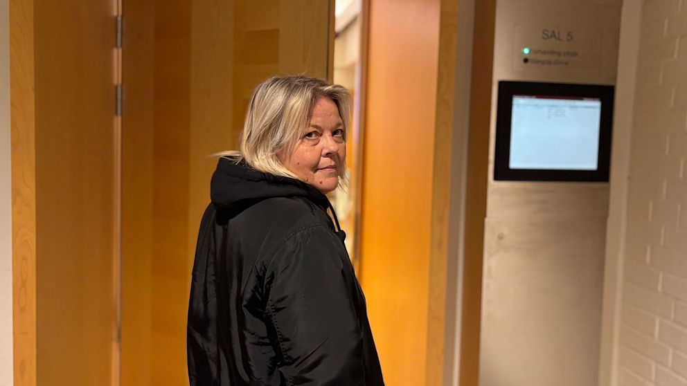 Person stårframför ett rum med en halvöppen dörr synlig i bakgrunden.