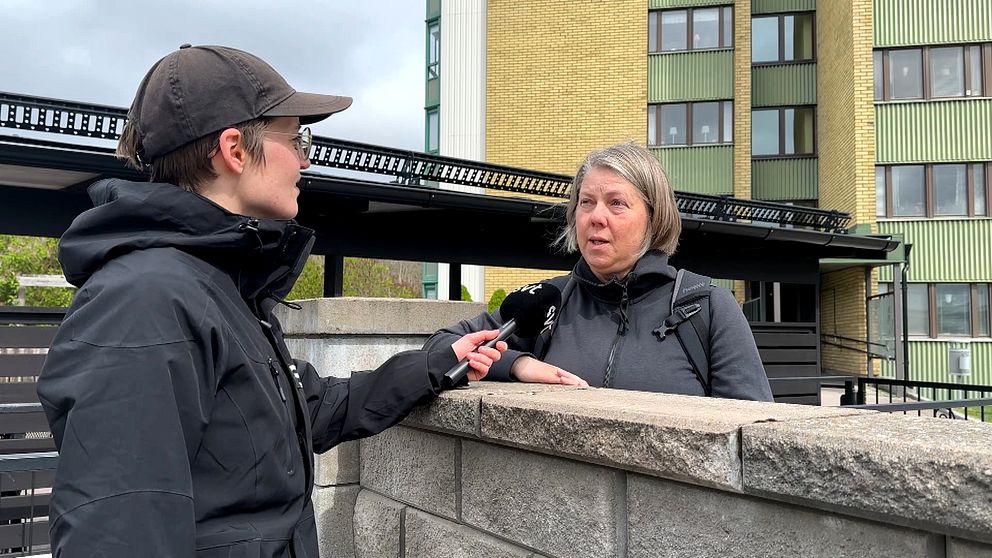 Reporter intervjuar en person vid en mur utanför ett flerbostadshus.