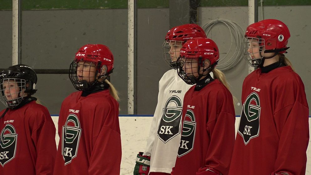 Flera tjejer står i hockeykläder och tittar ut från bild