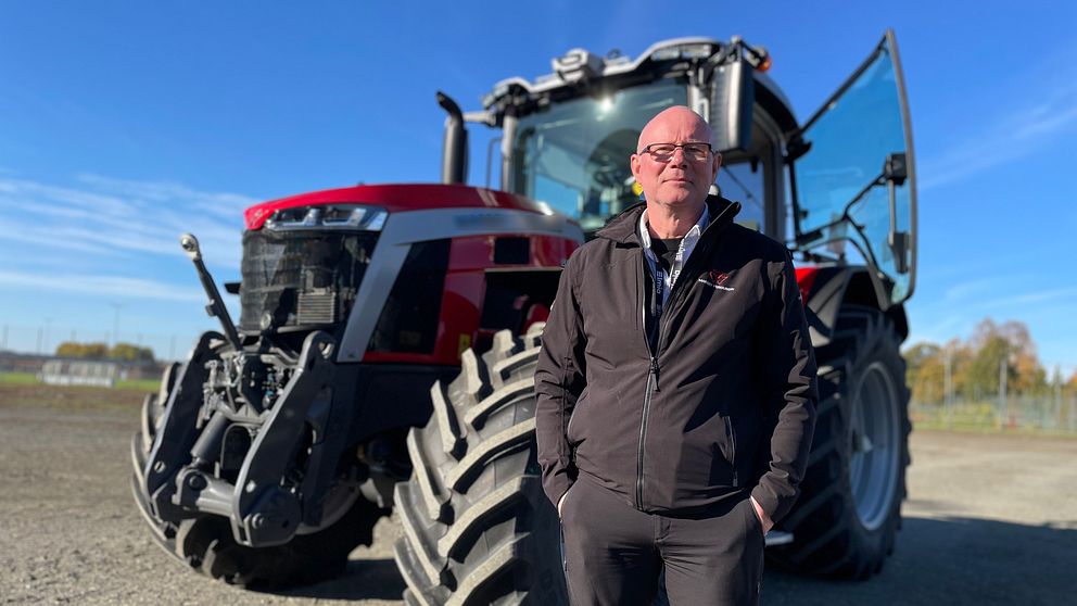 Självkörande traktor i ett öppet landskap. Traktorn har stora däck och är i gott skick, med förarhytten öppen. Himlen är klar och blå, vilket ger en ljus och solig atmosfär i bakgrunden.