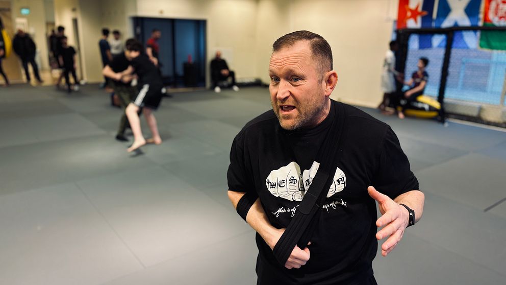Personer tränar kampsport i en dojo med grå mattor och flaggor på väggarna. I förgrunden Jörgen Hamberg, ordförande för Västerås fight club.