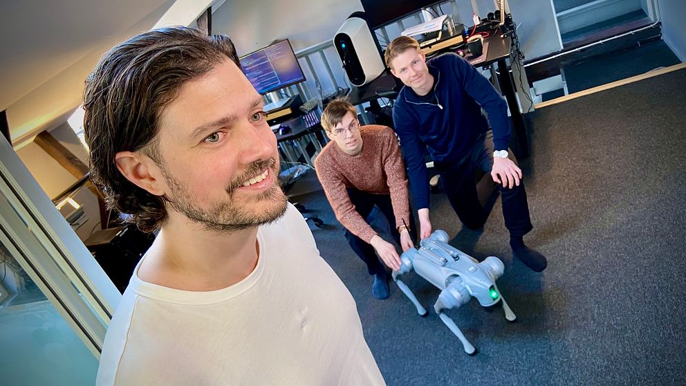 Två personer poserar med en fyrbent robot på ett kontor.